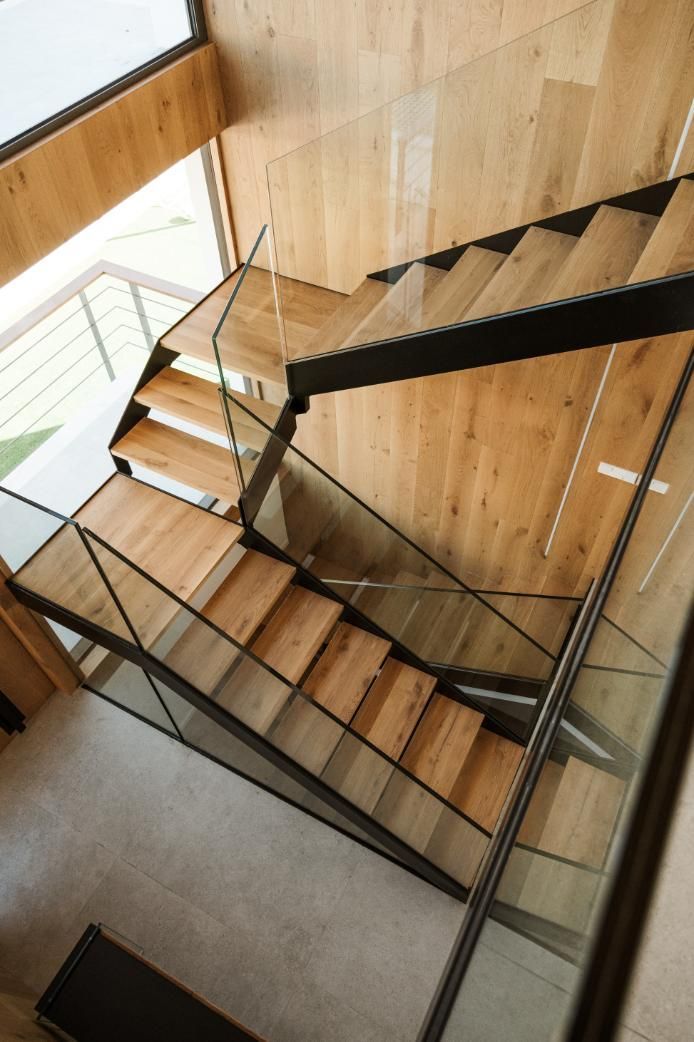 Escalera de madera con estructura de metal negro y paneles de cristal.