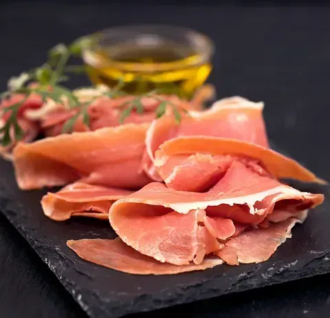 Unas lonchas de jamón están en una bandeja de pizarra junto a un bol con aceite de oliva.
