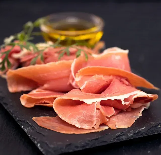 Jamón cortado en lonchas sobre una tabla de cortar de pizarra junto a un bol de aceite de oliva