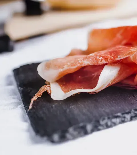 Un trozo de jamón reposa sobre una tabla de cortar de pizarra.