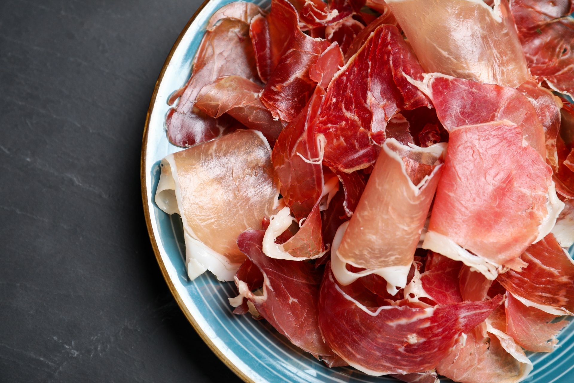 Un plato azul cubierto con jamón en rodajas sobre una mesa negra.