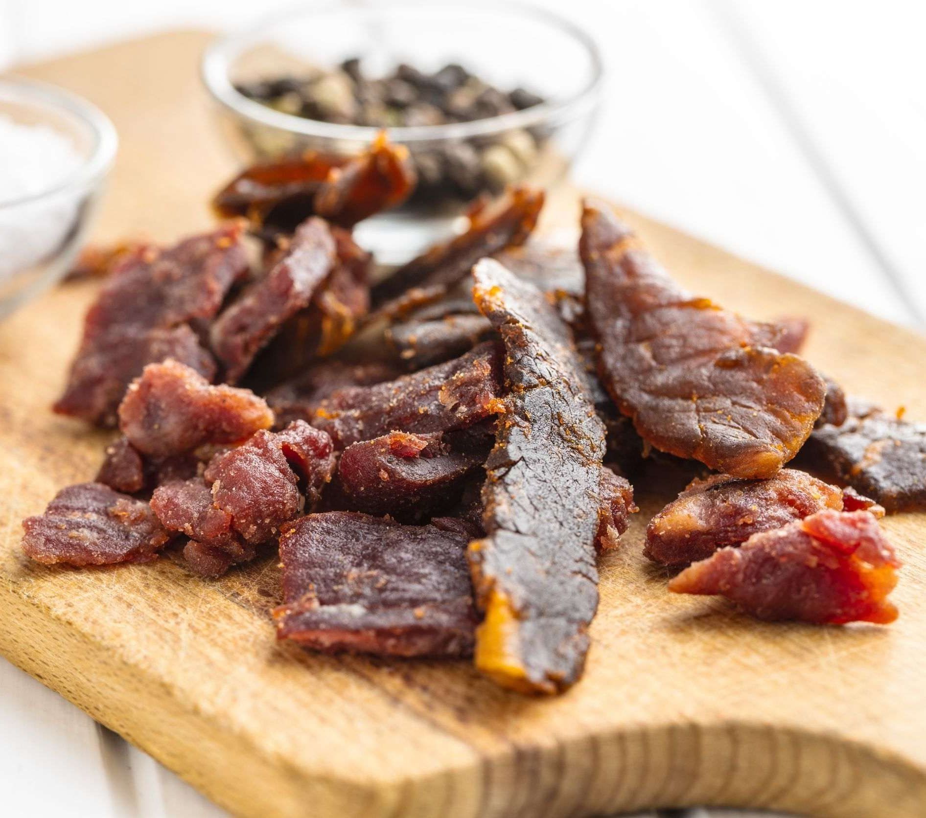 Una tabla de cortar de madera cubierta con carne seca junto a un tazón de pimienta.