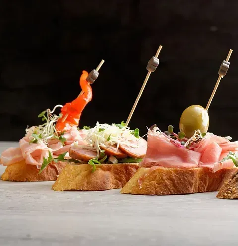 Tres bocadillos con carne y verduras en palillos sobre una mesa.