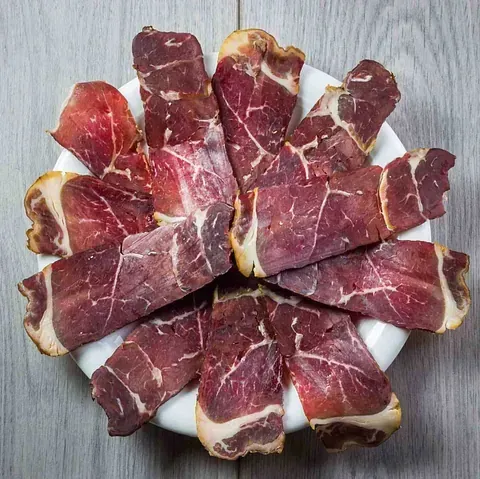 Un plato blanco cubierto con rodajas de carne sobre una mesa de madera.