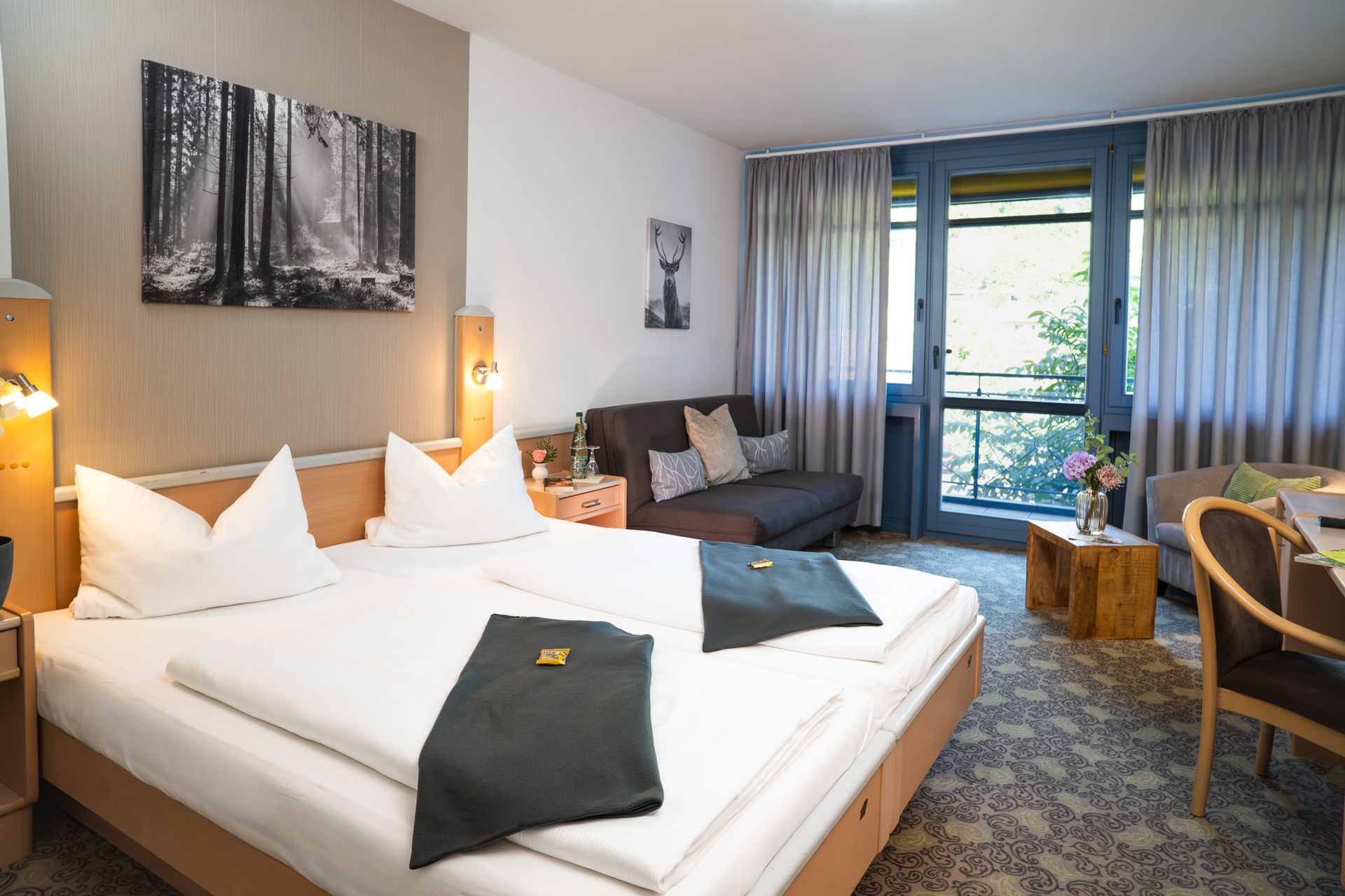 Hotelzimmer mit Bett, kleinem Sofa, Tisch und Fenster mit Blick auf Bäume.