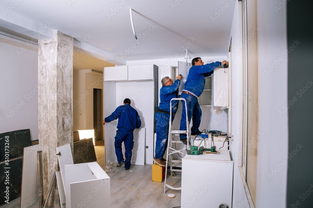 Arbeiter in blauen Overalls streichen einen Raum während einer Innenrenovierung.