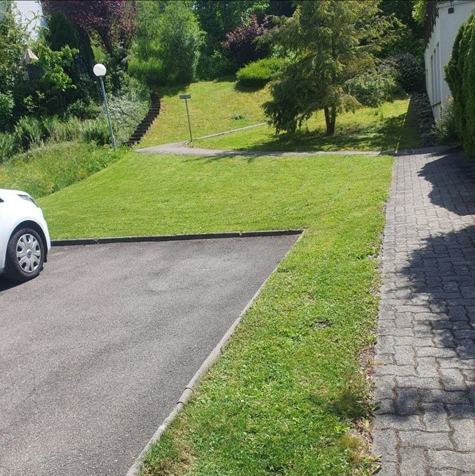 Ein Arbeiter benutzt ein Laubgebläse mit Rückentragegerät auf einer gepflasterten Strasse in der Nähe eines weissen Gebäudes.