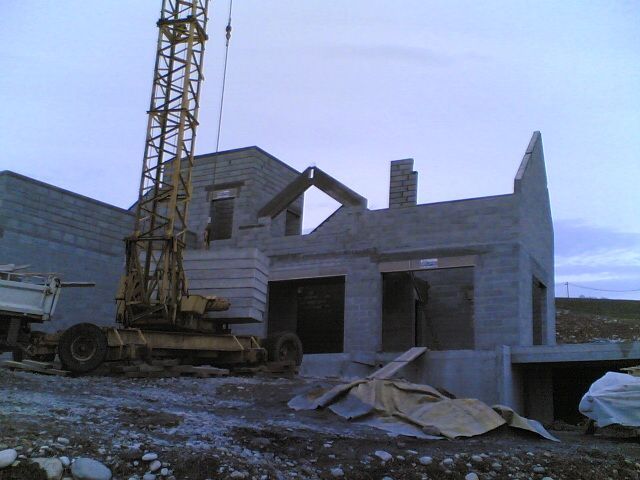 Chantier de construction d'une maison avec grue élévatrice au premier plan tandis que les murs s'élèvent petit à petit
