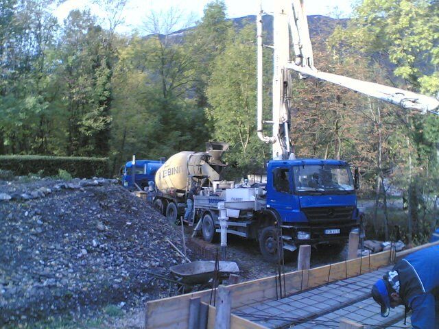 Bétonnière et bras-grue sur deux camions bleus à droite d'un talus rocheux