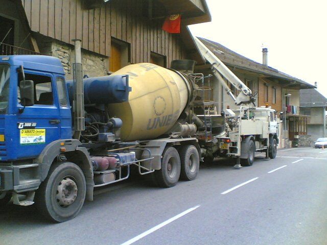 Bétonnière suivie d'un camion avec bras-grue pour une intervention en maçonnerie dans un habitat à étage