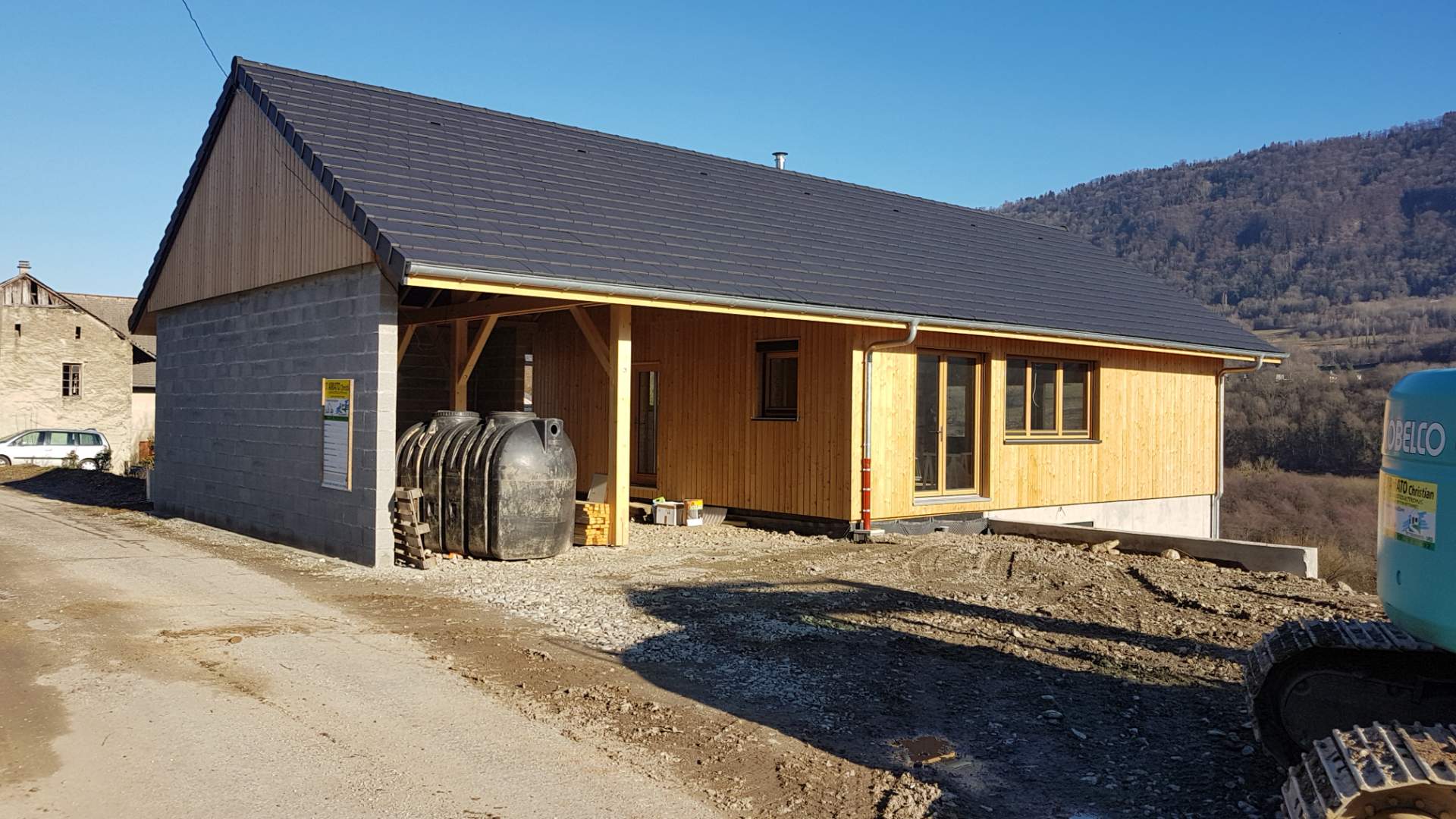 Chantier de construction d'une maison en bois avec fondation en ciment sous terre, et carport à gauche