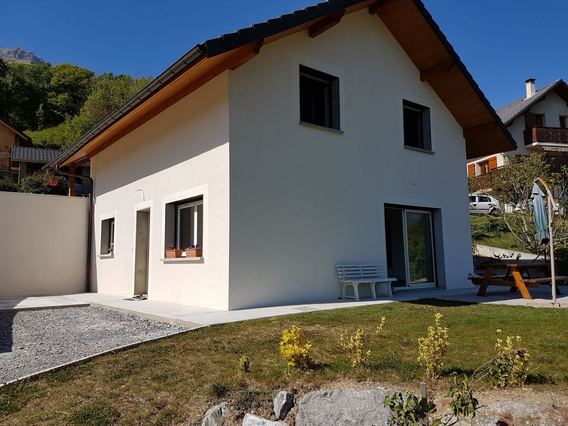 Pavillon construit aux murs blancs avec terrain gravillonné à gauche et jardin au premier plan
