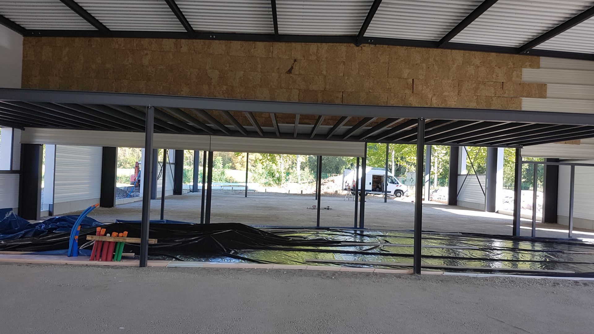 Vue intérieure d'un vaste édifice ouvert devant, aux structures métalliques dont le réseau électrique passe au milieu