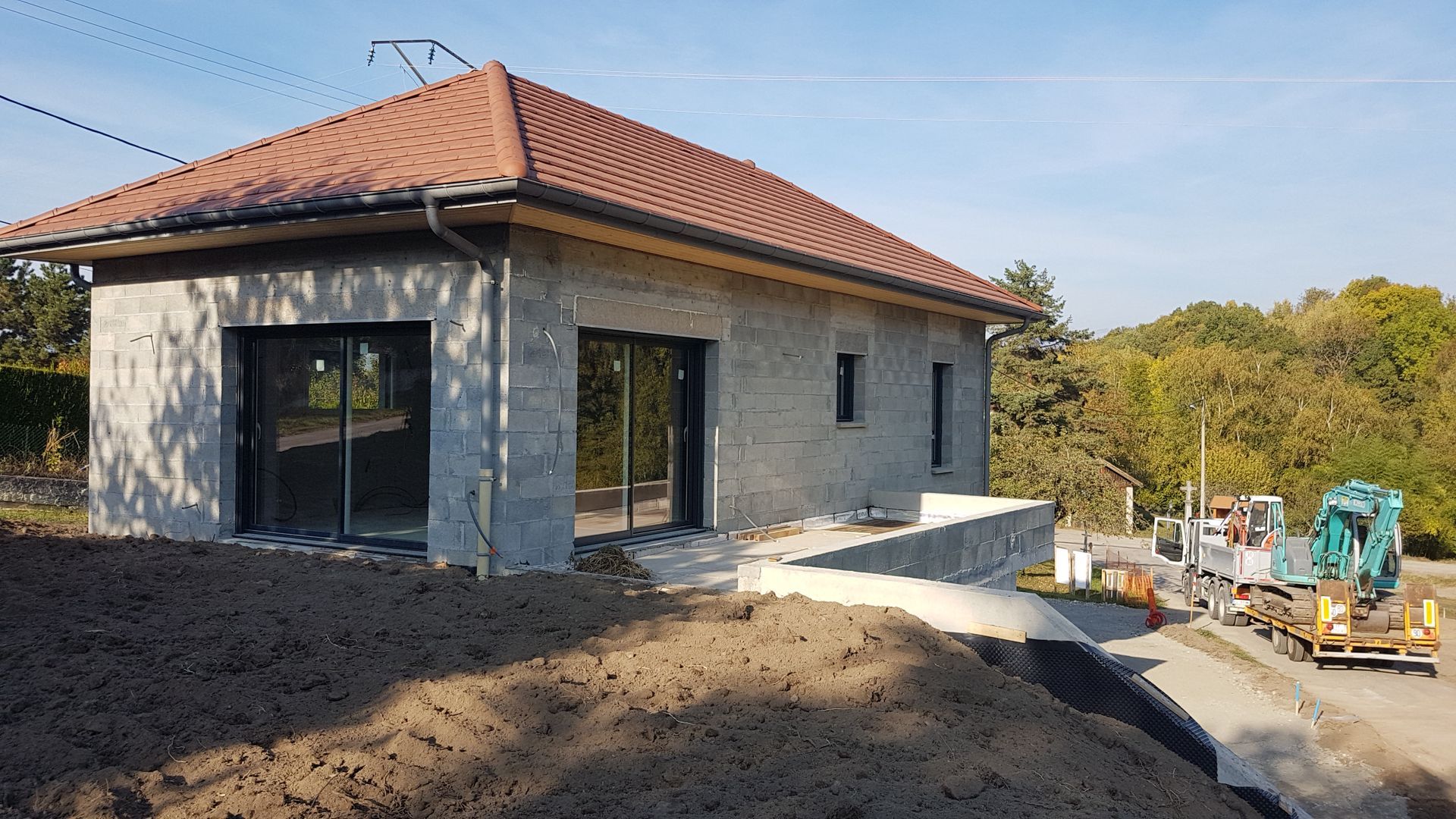 Chantier de construction d'une maison individuelle avec un terrassement au premier plan, un toit en tuile, des murs en béton