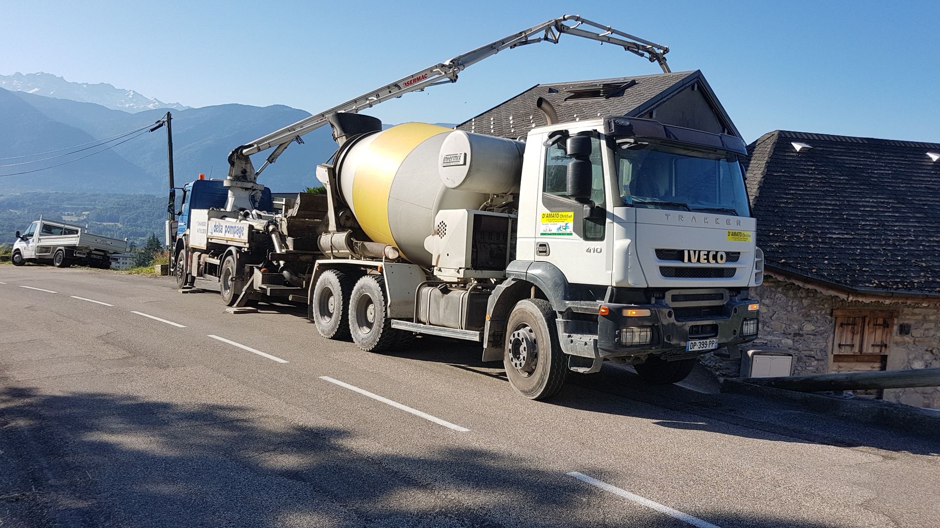 Camion avec un bras-grue en chantier de construction d'une maison avec une bétonnière placée devant