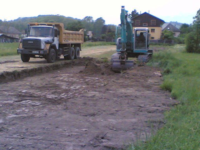 Travaux de terrassement à l'aide d'une tractopelle accompagnée d'un camion à benne sur la gauche