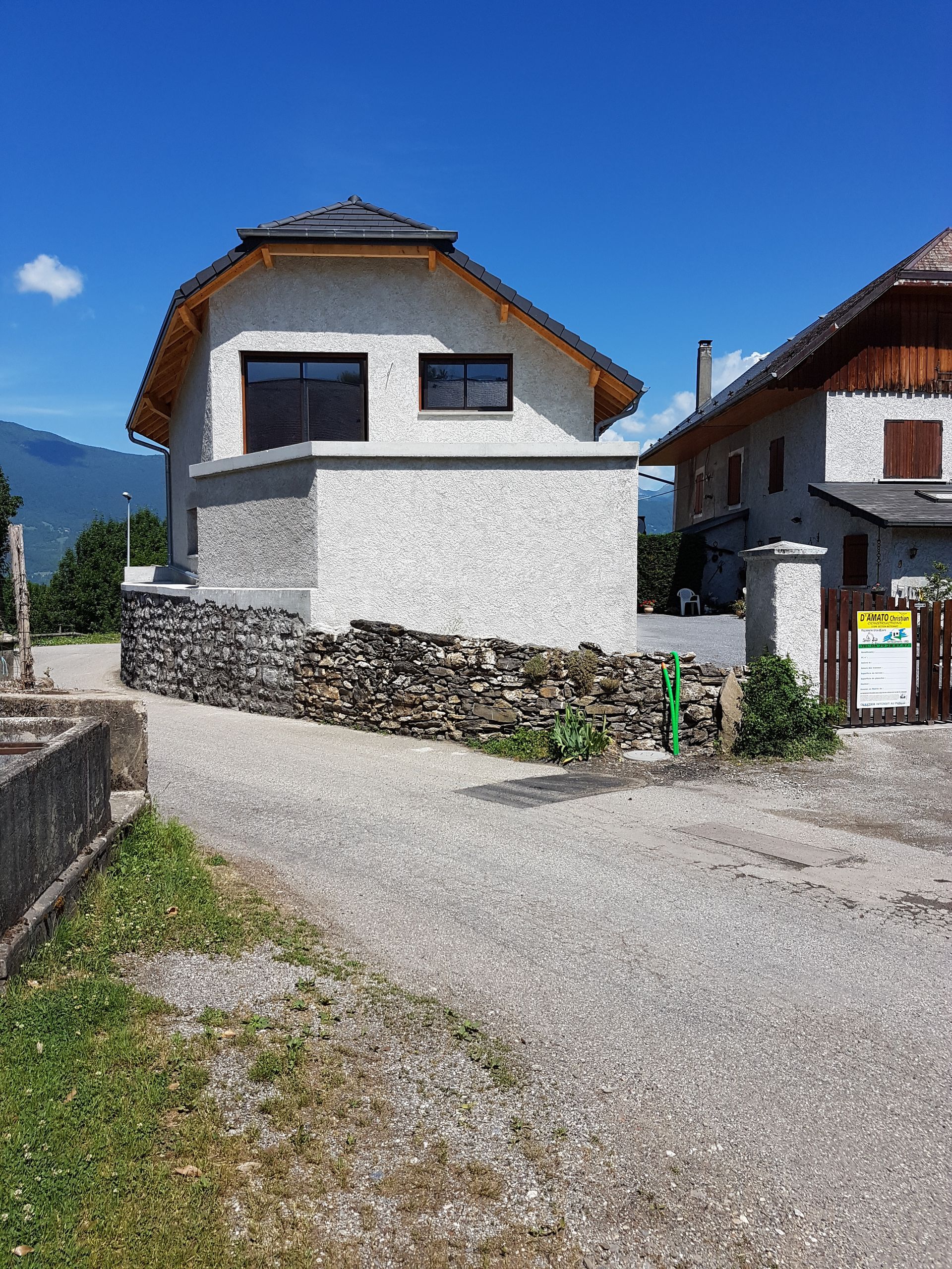 Vue large d'une construction aboutie d'une villa individuelle avec muret de pierre, portail à droite, étage et menuiseries