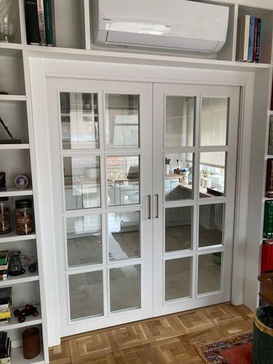 Puertas francesas blancas con múltiples paneles de vidrio, rodeadas de estanterías blancas, con un acondicionador de aire encima.
