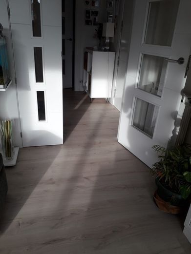Pasillo con suelo de madera, puertas blancas, luz del sol proyectando sombras.