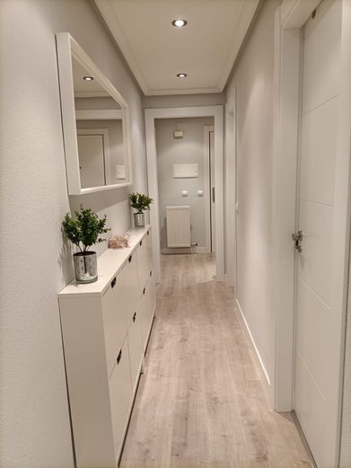 Pasillo estrecho con paredes blancas, suelo de madera clara y un armario blanco con espejo.