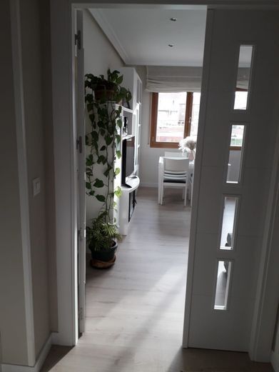 Puerta interior que conduce a una habitación muy iluminada con muebles blancos, plantas y una ventana.