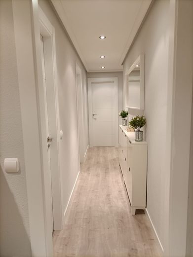 Pasillo estrecho con paredes blancas, suelo imitación madera clara y un armario blanco con espejo.