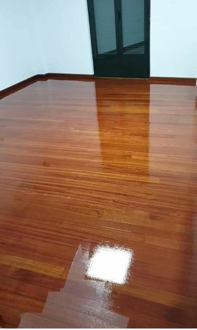 Suelo de madera brillante que refleja la luz, con una ventana oscura visible al fondo.