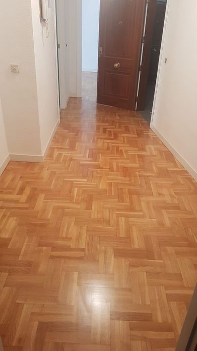 Pasillo con suelo de parquet, paredes blancas y puerta de madera.