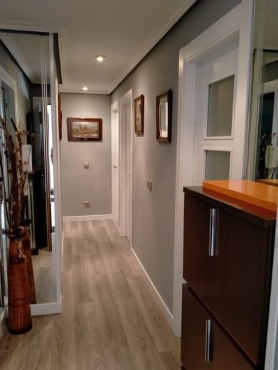 Pasillo largo con suelo imitación madera, paredes grises, puertas blancas y un zapatero. Pared con espejo a la izquierda.