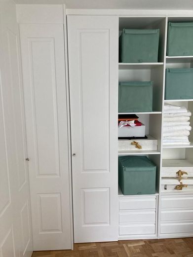 Armario empotrado blanco con puertas corredizas, estantes y cajas de almacenamiento de color verde azulado.