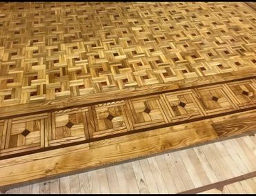 Suelo de parquet de madera con dibujo geométrico, bordeado por una banda decorativa.