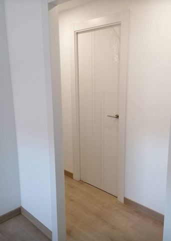 Puerta interior blanca en un pasillo estrecho con suelo de madera y paredes blancas.