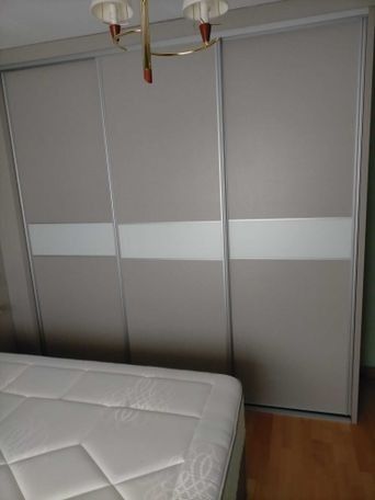 Un armario de puertas correderas de color beige con una raya blanca, junto a una cama con un colchón blanco, en el interior.