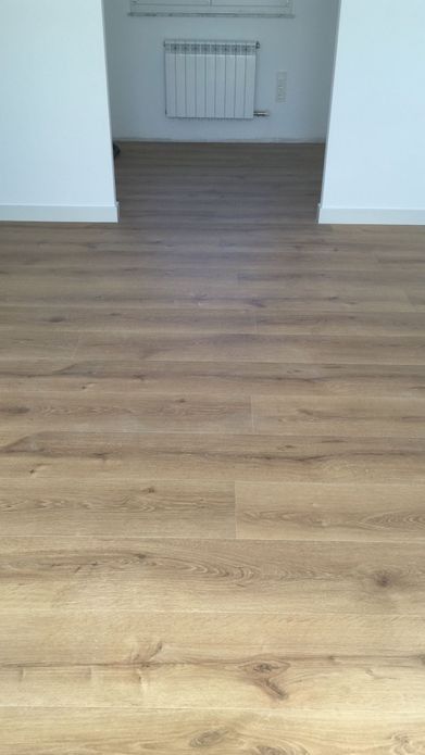 El suelo de madera se extiende hasta una puerta con un radiador al fondo. Las paredes son blancas.