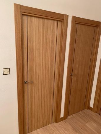 Dos puertas de madera en tono claro, colocadas en una pared de color claro con marcos a juego.