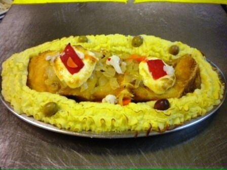 Prato saboroso com crosta de batata, recheado e decorado com azeitonas e pimentões, servido em uma chapa de metal.