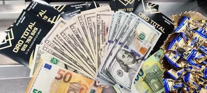 Billetes variados, lingotes de oro y bombones envueltos en papel dorado dispuestos en un expositor de dinero.