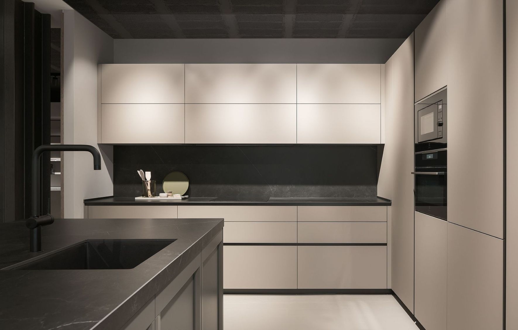 Cocina moderna minimalista con encimeras negras, armarios beige y horno empotrado.