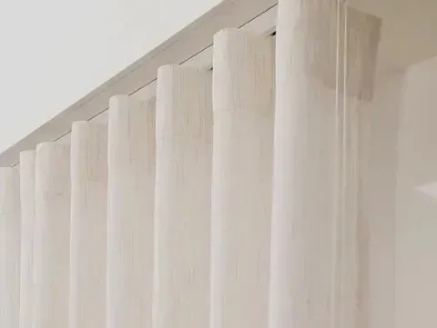 Primer plano de unas cortinas blancas plegables en forma de S, que llegan hasta el suelo y cuelgan de un riel.