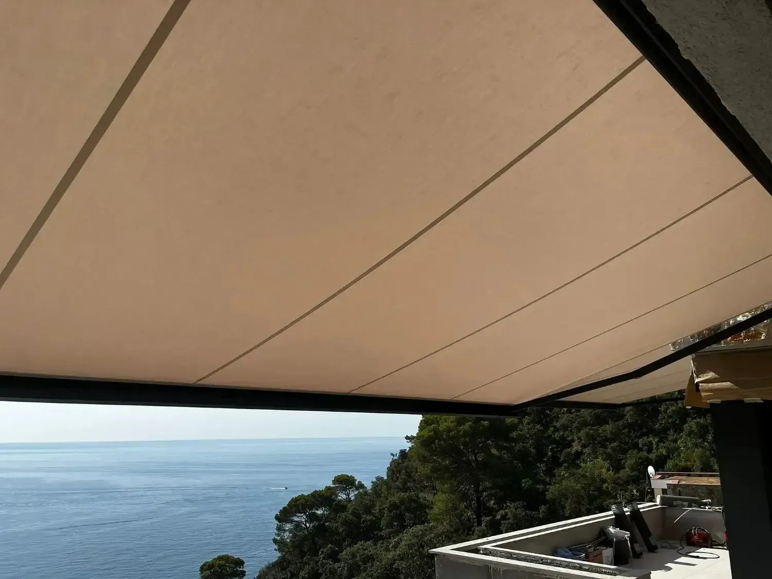 Un toldo retráctil de color beige se extiende sobre un balcón costero con vistas al mar y a los acantilados verdes.