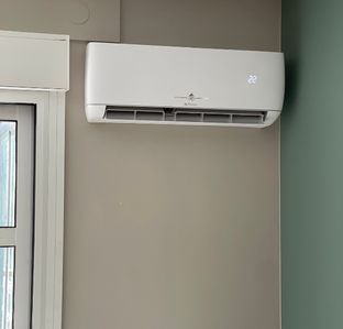Climatiseur blanc fixé sur un mur beige avec affichage numérique de la température. Coin avec mur végétalisé.