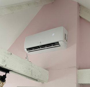 Climatiseur blanc monté sur un mur rose dans une pièce avec poutres apparentes.