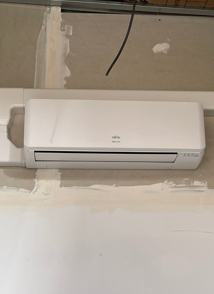 Climatiseur blanc monté sur un mur clair. Un fil noir est suspendu au-dessus.