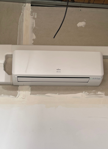 Climatiseur blanc monté sur un mur clair. Un fil noir est suspendu au-dessus.