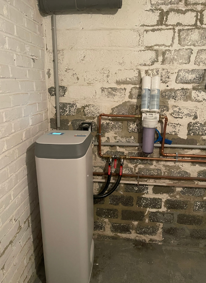 Un système d'adoucisseur d'eau et un filtre fixés à des tuyaux en cuivre sur un mur de sous-sol en briques.