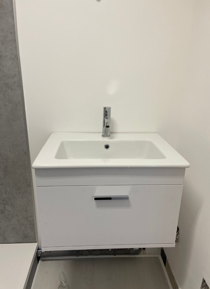 Meuble-lavabo blanc avec lavabo et robinet à poignée unique, avec un tiroir et un fond blanc.