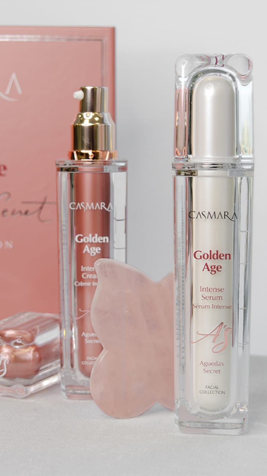 Dos botellas de cuidado de la piel, una herramienta Gua Sha y un libro, sobre un fondo blanco.