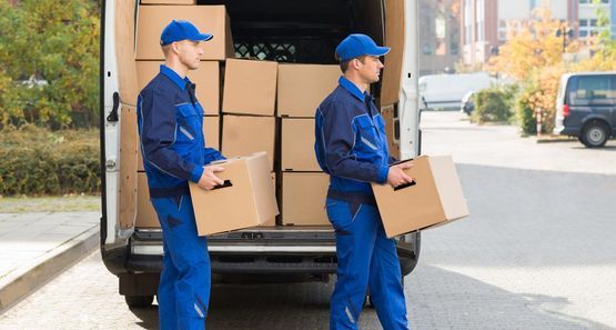 Dos repartidores con uniformes azules descargan cajas de un camión.