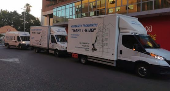 Una fila de camiones de mudanza blancos estacionados frente a un edificio al anochecer, con grandes textos en sus laterales.
