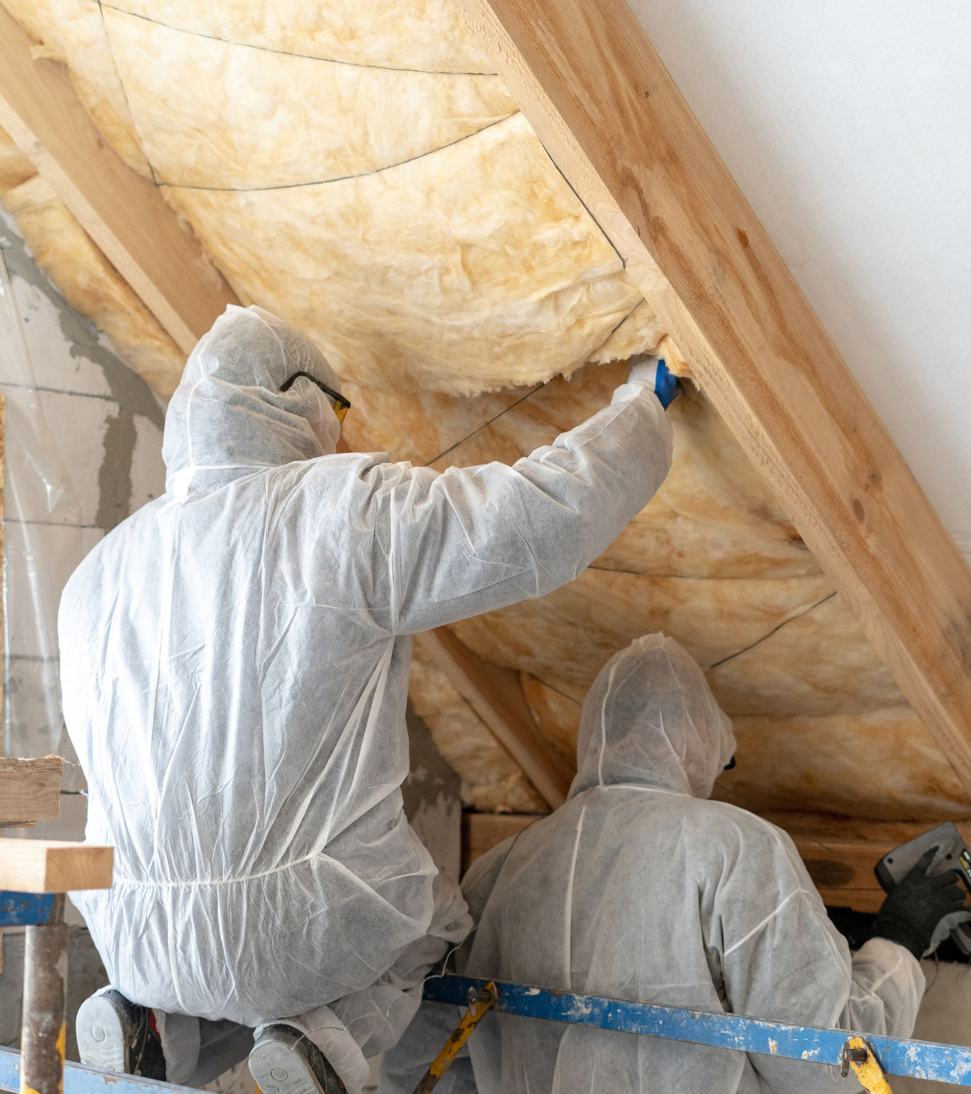 Deux personnes en combinaisons de protection installent de l'isolant dans un grenier.
